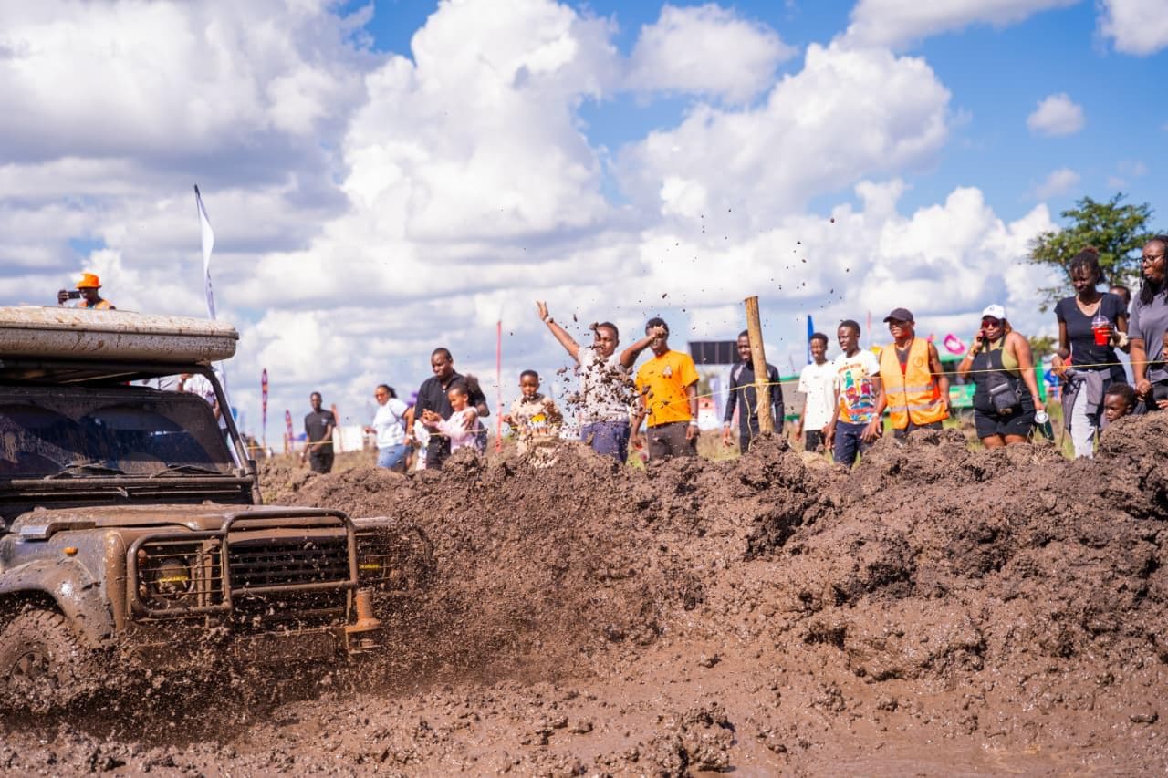 A mud-caked 4x4 crawling over a mound of earth as a cheering crowd of spectators lines the course