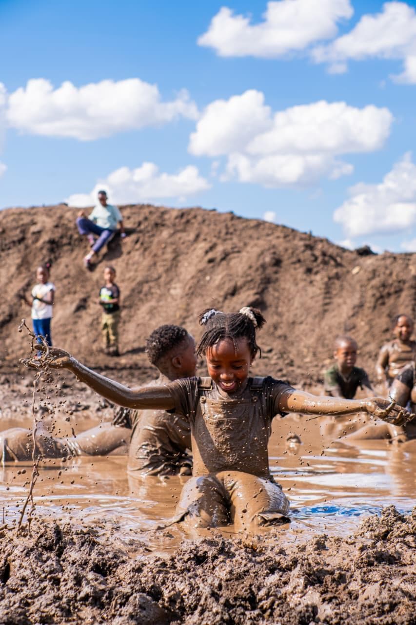 A girl mid-splash in a mud pit, other kids playing around her