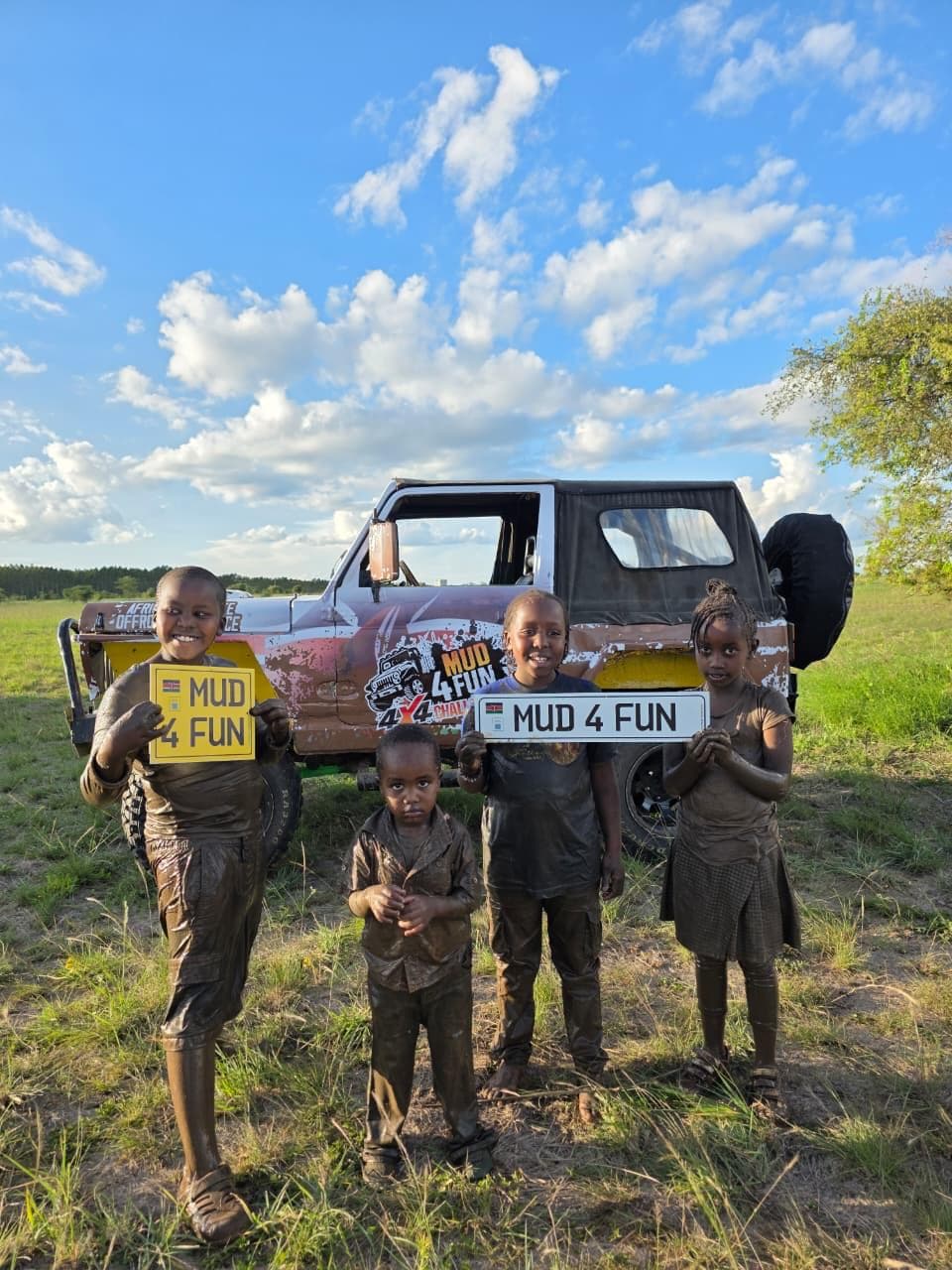 Four mud-caked kids holding Mud4Fun number plates in front of a 4x4