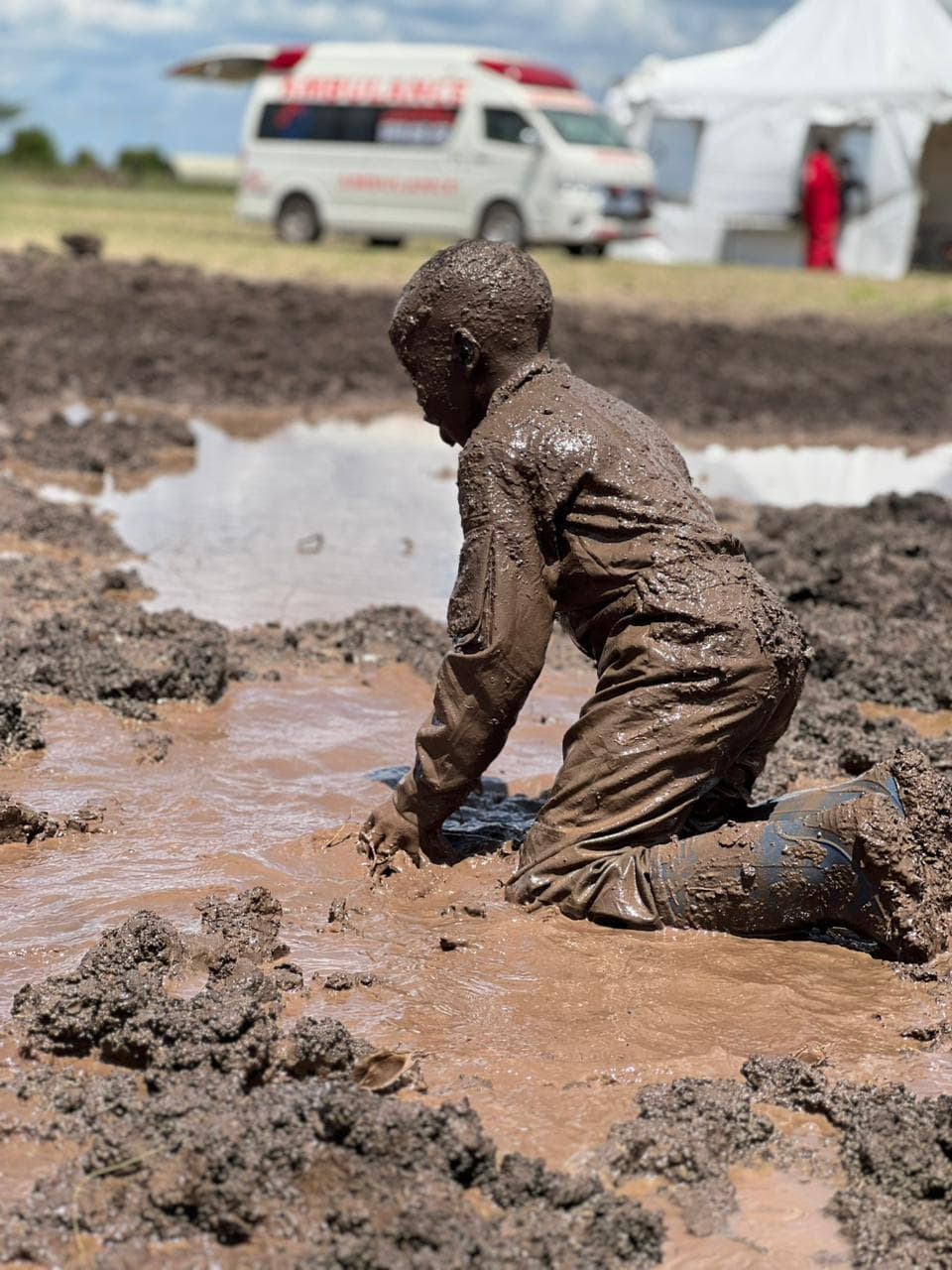 A boy kneeling in a muddy puddle, mud-caked from head to toe