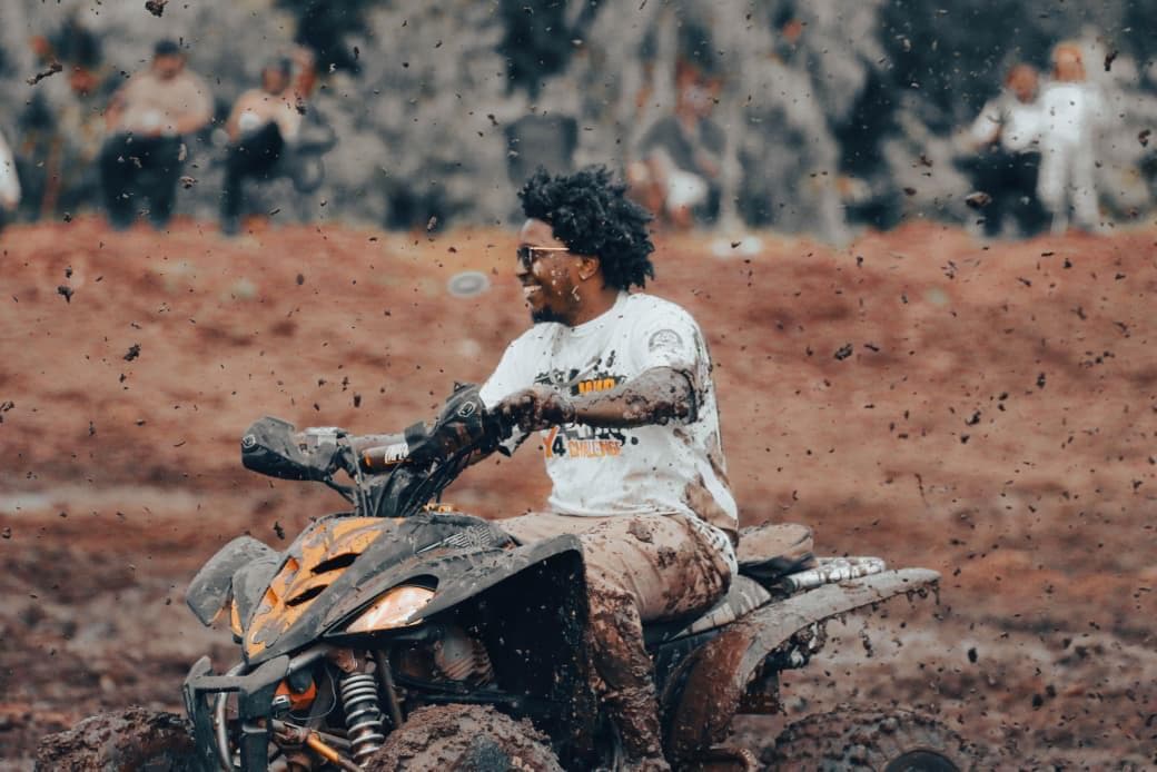 A grinning quad bike rider wearing a Mud4Fun 4x4 Challenge shirt, covered in flying mud